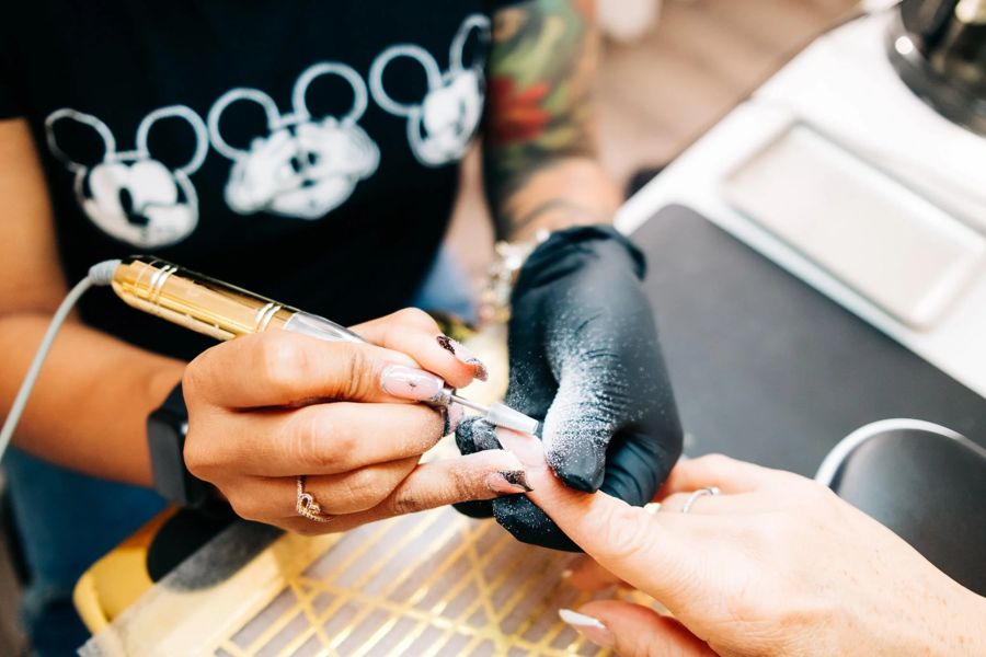 Thiara shaping a client set with an electric file, gloved, during a private appointment at TLC Nails and Esthetics in Nottingham, MD