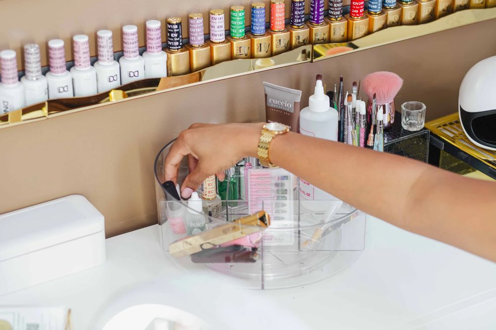 Thiara reaching for hand files and prep tools at her nail station at TLC Nails and Esthetics in Nottingham, MD, next to the gel polish wall used after a nail removal
