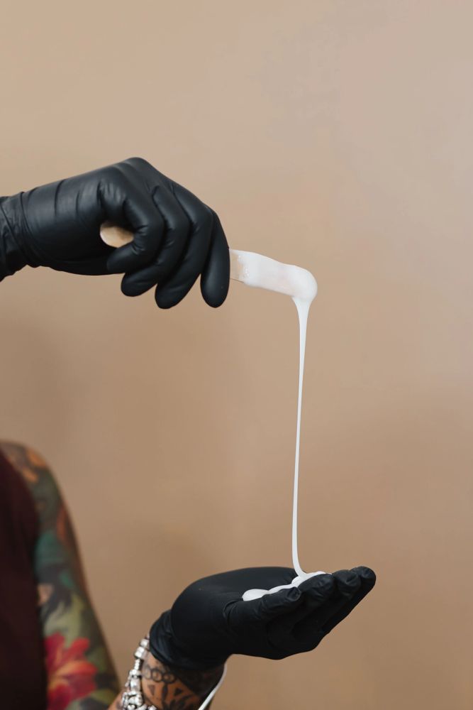 Gloved hands checking the consistency of warm soft wax on a spatula before a bikini wax at TLC Nails and Esthetics in Nottingham, MD