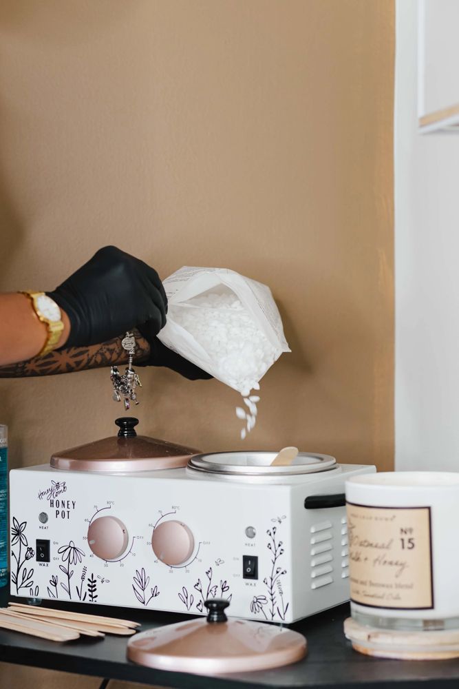 Gloved hand pouring hard wax beads into the double wax warmer before an extended bikini wax at TLC Nails and Esthetics in Nottingham, MD
